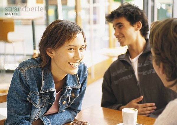 Gruppe junger Leute sitzt am Tisch im Café  lächelnd