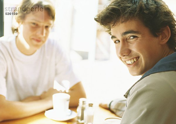 Zwei junge Männer sitzen am Tisch und lächeln.