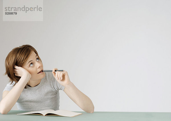 Junge Frau sitzend mit geöffnetem Notizbuch  hält Bleistift an den Mund