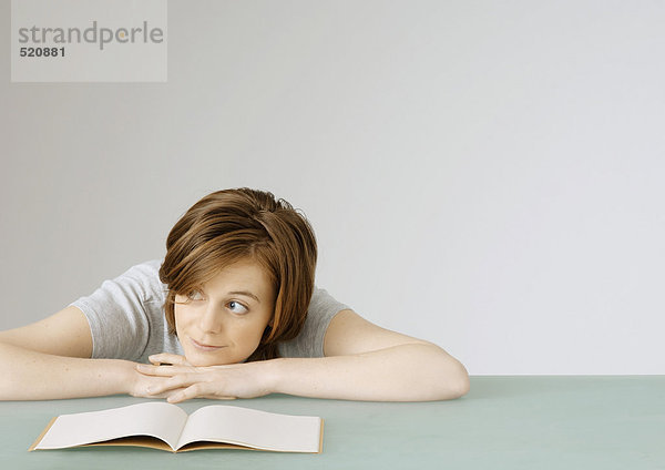 Junge Frau sitzend mit Kopf auf Tisch neben offenem Notizbuch