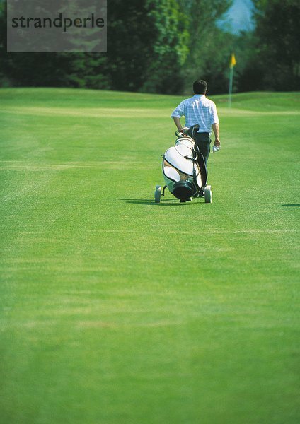 Golfer zieht Golftasche auf Grün
