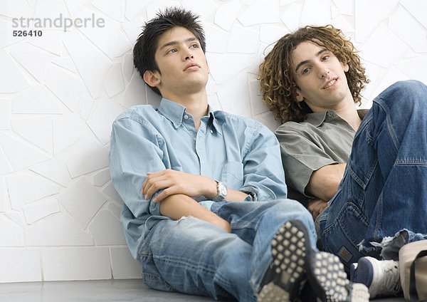 Zwei junge Männer sitzen auf dem Boden und lehnen sich an die Wand.