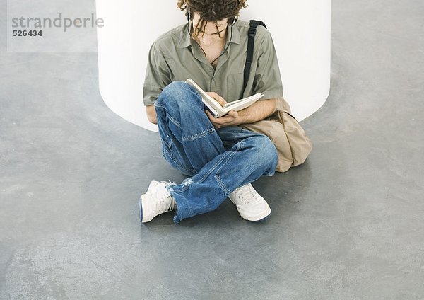 Junger Mann auf dem Boden sitzend  lesend