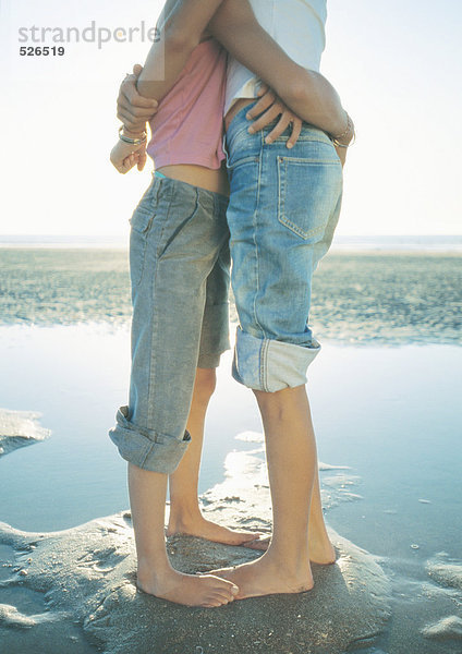 Zwei Kinder stehen am Strand und umarmen sich.