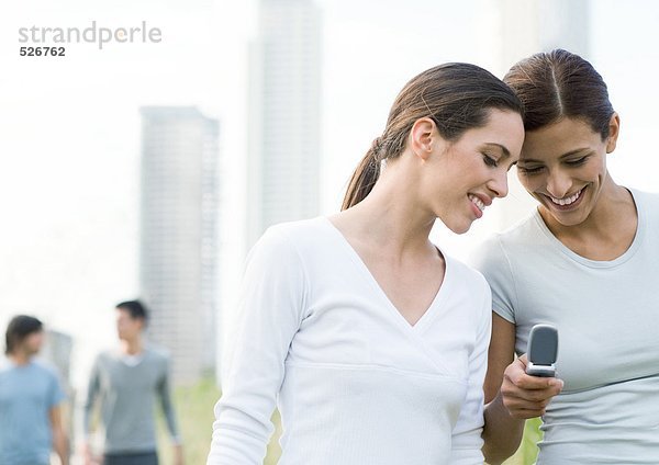 Zwei junge Frauen  die auf das Handy im Stadtpark schauen