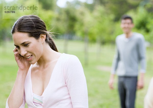 Junge Frau spricht am Handy  Mann im Hintergrund  im Park