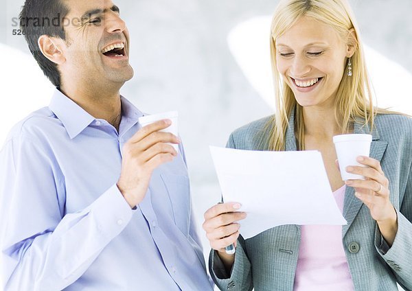 Geschäftsmann und Geschäftsfrau halten Tassen und lachen über Dokument