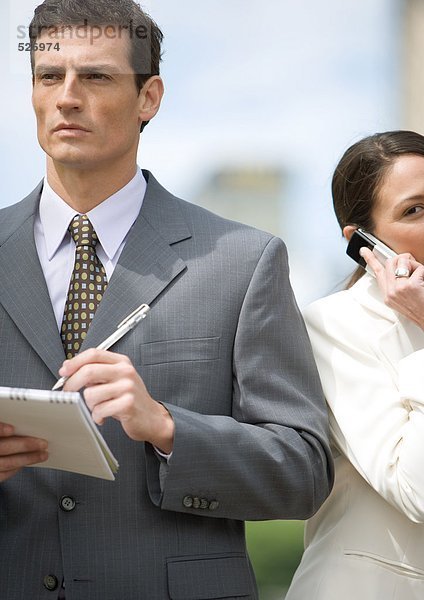 Geschäftsmann macht sich Notizen  während die Geschäftsfrau das Handy benutzt.