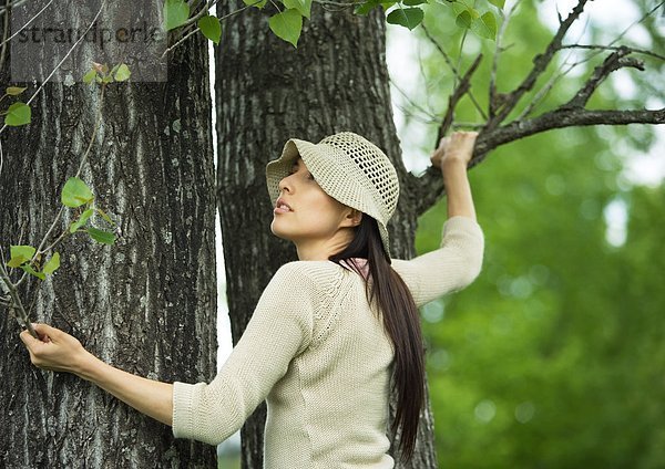 Junge Frau hält sich am Baum fest
