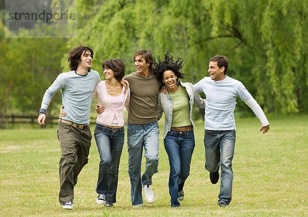 Gruppe junger Freunde  die sich umarmen und über das Feld springen.