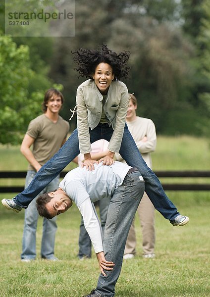 Junge Frau  die mit einem jungen Mann springt  während Freunde zuschauen.