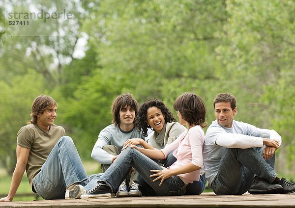 Gruppe junger erwachsener Freunde  die zusammen draußen sitzen.