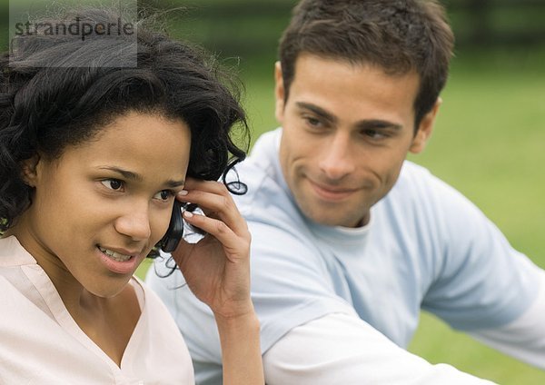 Junge Frau benutzt Handy  während der junge Mann zuhört.