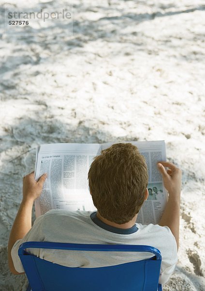 Mann sitzt im Strandkorb und liest Zeitung  Rückansicht