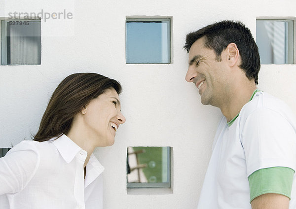 Frau und Mann  beide an die Wand gelehnt  mit quadratischen Fenstern und lächelnd.