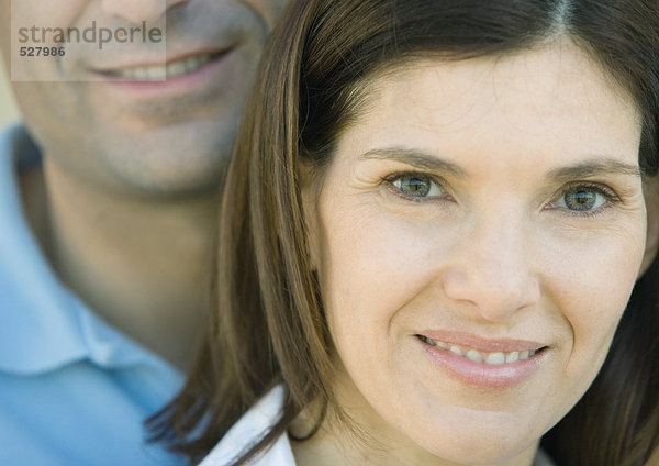 Frau lächelt und schaut in die Kamera mit ihrem Mann hinter sich  Porträt  extreme Nahaufnahme