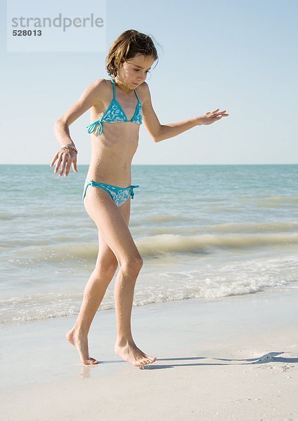 Mädchen am Strand  auf Zehenspitzen vom Wasser weggehen
