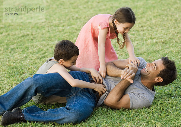 Junge und Mädchen kitzeln Vater auf Rasen