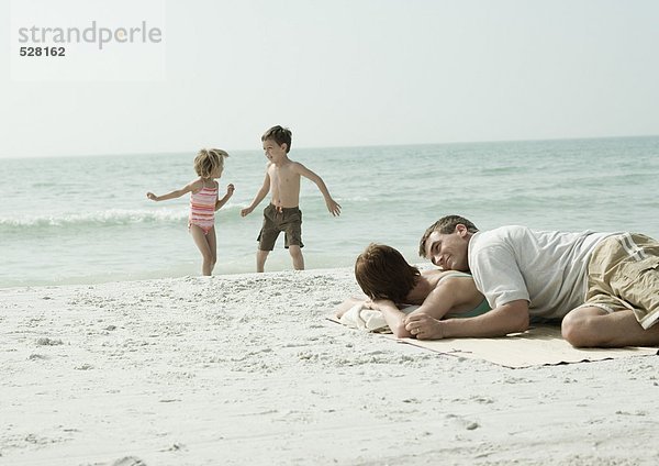 Eltern liegen am Strand  Kinder spielen im Hintergrund