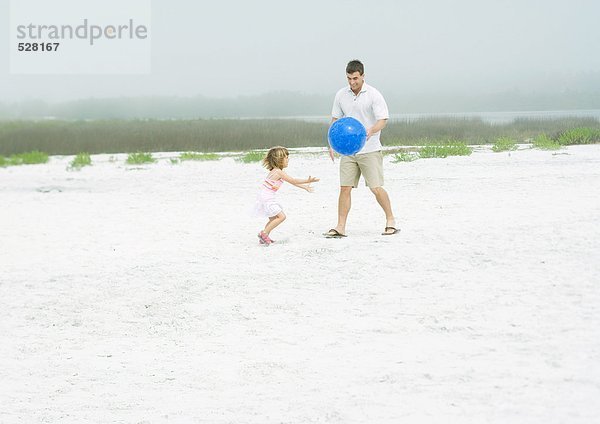 Mann spielt Ball mit Tochter auf Sand