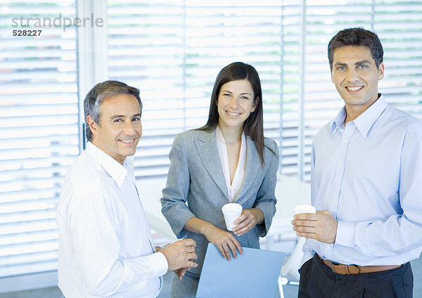 Drei Geschäftskollegen im Büro mit Tassen in den Händen  lächelnd vor der Kamera.