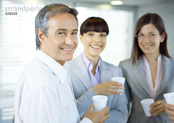 Geschäftskollegen im Büro mit Tassen in der Hand  lächelnd vor der Kamera