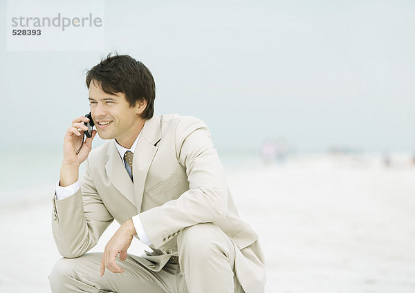 Geschäftsmann am Strand hockend  mit dem Handy