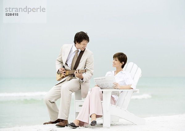 Geschäftsmann spielt Streichinstrument für Frau am Strand