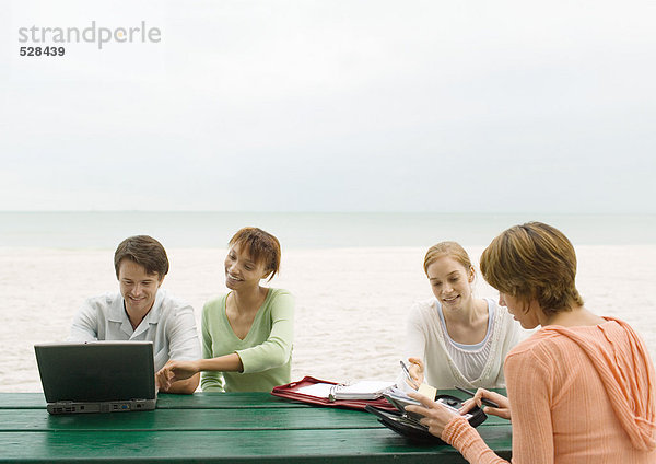 Vier Erwachsene am Picknicktisch am Strand mit Blick auf Laptop und Agenden
