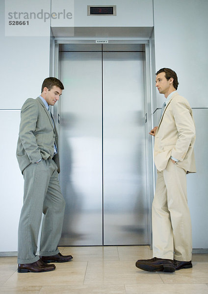 Zwei Geschäftsleute warten an der Aufzugstür.