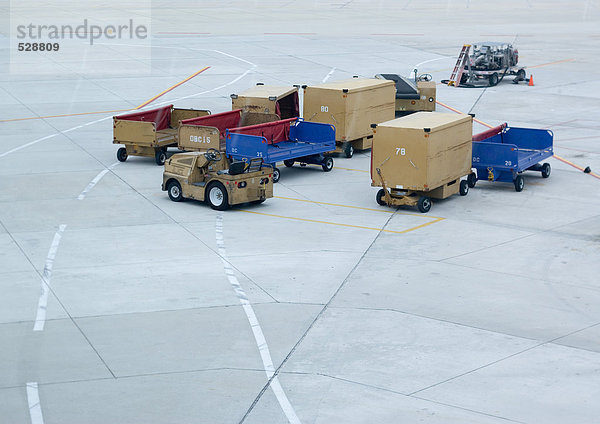 Gepäckwagen und Container auf der Landebahn des Flughafens