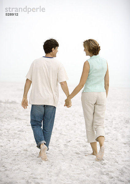 Erwachsenes Paar  das am Strand spazieren geht  Händchen haltend  Rückansicht