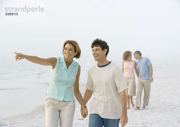 Ein reifes Paar  das am Strand spazieren geht  eine Frau  die in die Ferne zeigt.