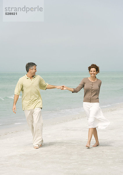 Ein reifes Paar  das am Strand spazieren geht und Händchen hält.