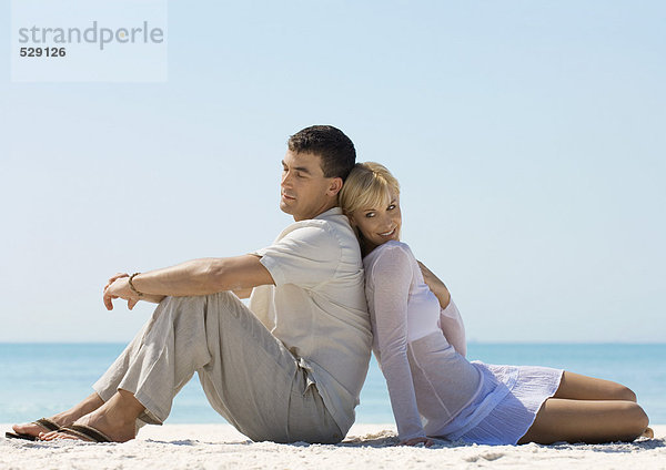 Paar sitzt Rücken an Rücken am Strand