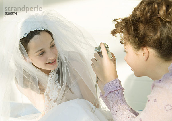 Preteen Mädchen beim Fotografieren eines Freundes im Hochzeitskleid