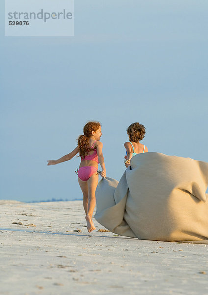 Zwei Mädchen mit Decke im Wind am Strand