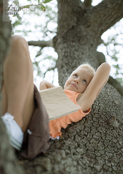 Mädchen im Baum liegend mit Buch auf dem Bauch