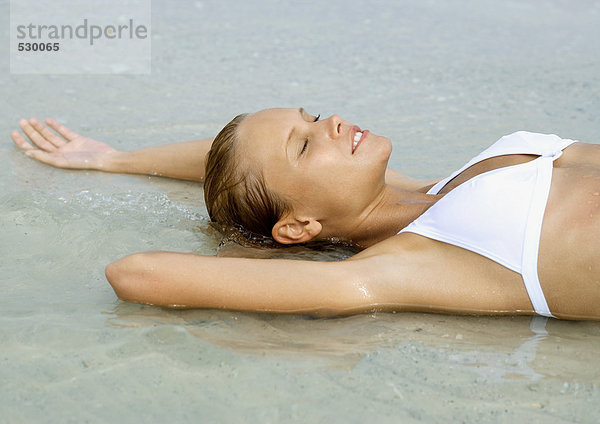 Frau im flachen Wasser am Strand liegend  Augen geschlossen