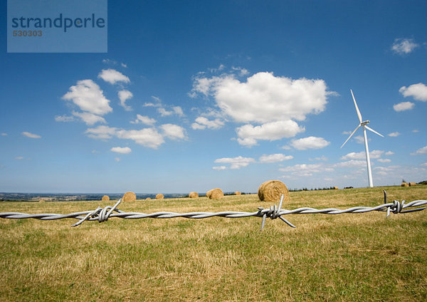 Windkraftanlage im Feld mit Heuballen  Stacheldraht im Vordergrund