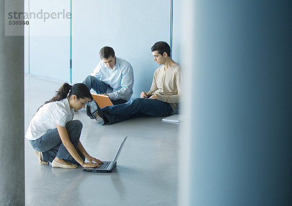 Junge Frau und zwei junge Männer mit Laptops auf dem Boden