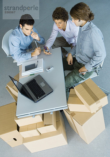 Geschäftsleute  die an der Tischplatte sitzen und von Kartons gestützt werden  hohe Blickwinkel