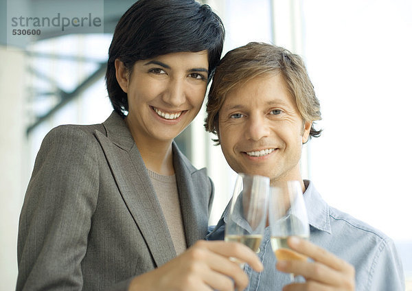 Professioneller Mann und Frau klirren mit Champagner  lächeln in die Kamera.