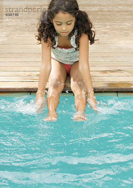 Mädchen am Beckenrand sitzend mit Händen und Füßen im Wasser