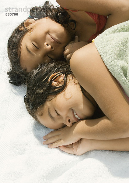 Zwei Mädchen liegen zusammen  eine in ein Handtuch gewickelt.