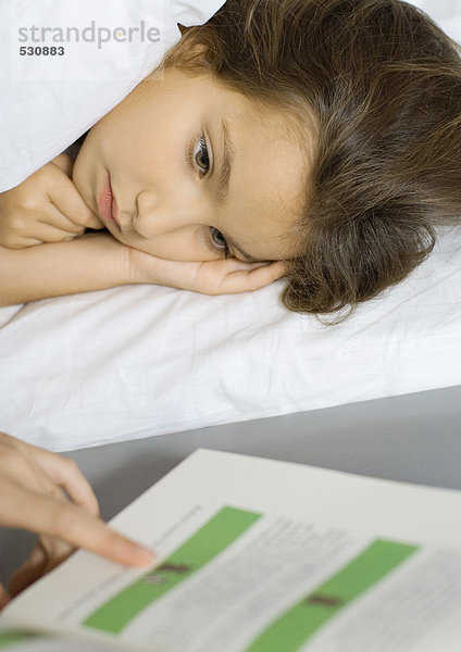 Mädchen im Bett liegend  Mutter beim Lesen aus dem Buch zuhörend