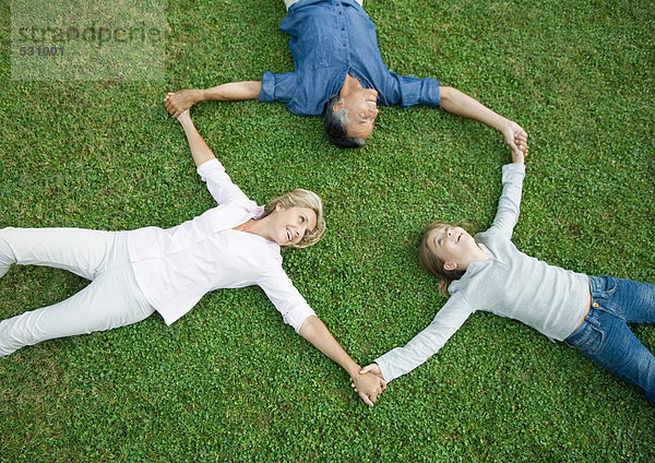 Erwachsenes Paar und Enkelin auf Gras liegend  Händchen haltend