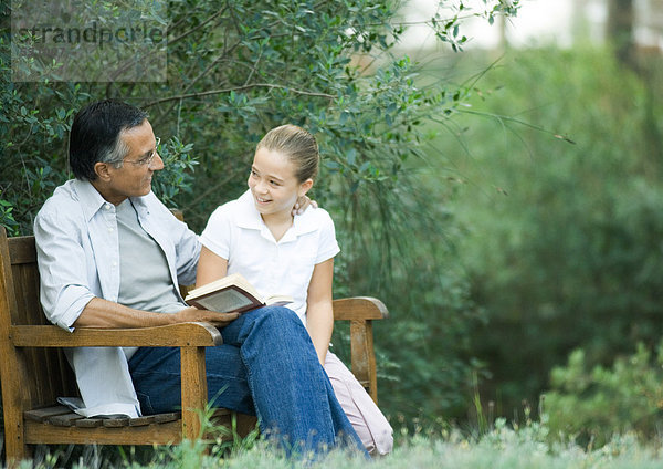 Erwachsener Mann beim Lesen mit Enkelin im Freien