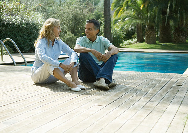 Reife Paare sitzen an Deck am Swimmingpool