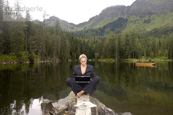 Geschäftsfrau am See sitzend mit Laptop